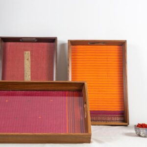 Left vertical: A beautiful, antiquated palm leaf scripture on a red tissue silk in a 100 year old Burma teak frame. Right vertical: A Fanta orange striped Kanchipuram silk with a typical maroon zari border with traditional motifs in a 100 year old Burma teak frame. Front horizontal: A 100 year old Burma teak frame inlaid with a cherry coloured thread work Kanchipuram silk.