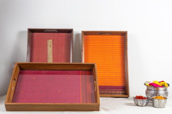 Left vertical: A beautiful, antiquated palm leaf scripture on a red tissue silk in a 100 year old Burma teak frame. Right vertical: A Fanta orange striped Kanchipuram silk with a typical maroon zari border with traditional motifs in a 100 year old Burma teak frame. Front horizontal: A 100 year old Burma teak frame inlaid with a cherry coloured thread work Kanchipuram silk.